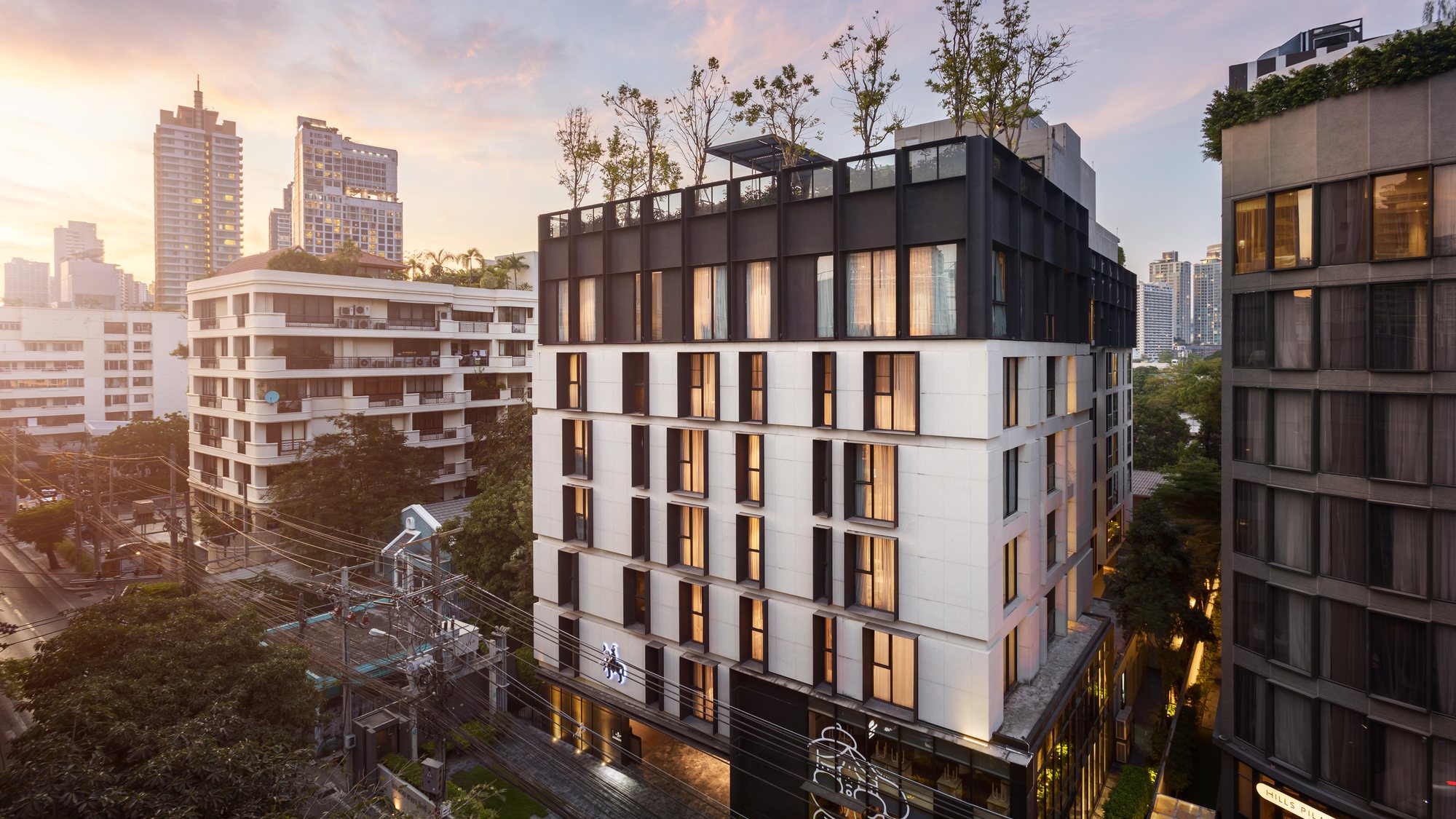 Walton Suites exterior and Bangkok skyline at sunset